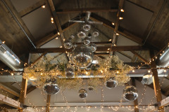 view of the top of the barn on the inside featuring disco balls and floral hanging from rafters and guidewire.