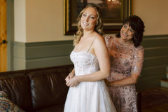 bride being buttoned into dress by mother of bride while staring off into the distance