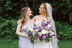 bride and bridesmaids in purple holding flowers and looking at each other.