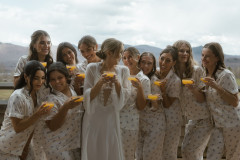 bride with bridal party in matching outfits all holding glasses of orange liquid. 