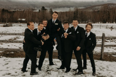bride being lifted up by groomsmen in front of wooden fence with mountain scape in the background.