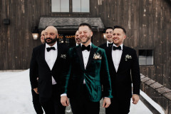 groom and groomsmen walking towards camera in black and green tuxedos with floral pocket squares.