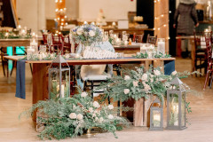 bride and groom sweetheart table with greenery and lanterns surrounding it in the event barn.