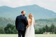 bride and groom standing in front of meadow and mountains.