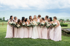 bride standing in middle with eleven bridesmaids in pink dresses all holding wedding bouquets.