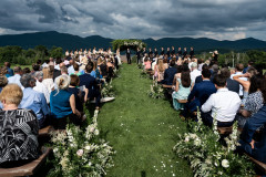 wedding knoll featuring guests sitting around on farmhouse benches with mountains in the background.