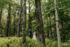 bride and groom in woods holding hands.