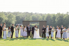 bride and groom kissing at barn doors with wedding party surrounding them.