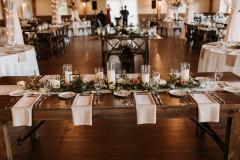 table setting on a farmhouse table with white linens with greenery and candles in the middle.