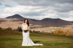 bride standing in front of mountain scape in the fall holding a bouquet of white florals.