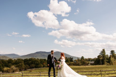 bride and groom standing together in front of camera with wooden fence behind them and green mountain landscape. 