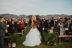 bride and groom kissing in front of ceremony arbor with guests standing around them with mountain scape in background.