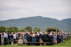 bride and groom at wedding arbor overlooking mountains with guests at farmhouse benches.
