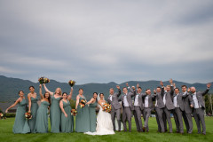 bride and groom in center surrounded by wedding party with wedding bouquets and mountainscape in the background.