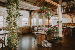 interior of event barn decorated with wedding florals and roses with drapery and disco balls hanging from rafters.