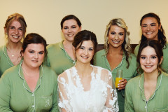 bridesmaids in green robes surrounding bride in white robe.