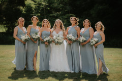 bride and 6 bridesmaids standing in line holding floral bouquets.
