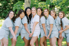 bride holding hands with bridal party featuring seven women in light blue