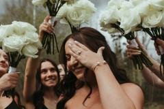 bride hiding her face to show her ring and bridesmaids standing around her showing off the bouquets.