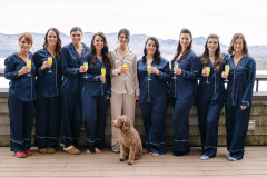 photo of bride and eight bridesmaids and dog. women holding mimosas with winterscape behind them.