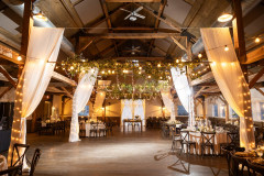 interior of event barn featuring cathedral style drapes, round tables, and greenery.