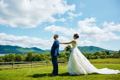 first look photo of bride tapping shoulder of groom in field with wooden fence and mountains in background.