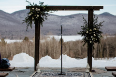 wedding arbor with floral designs on it with rug on terrace with mountain scape in background.