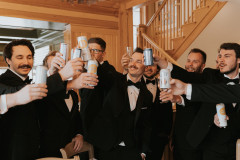 groom and groomsmen in black suits holding drinks and cheersing together.