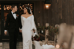 bride and groom walking away from event barn doors with wooden fence lined with garland on their left hand side (right side of photo).