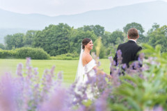 bride and groom walking in field with lavender scape in front and mountains in background.