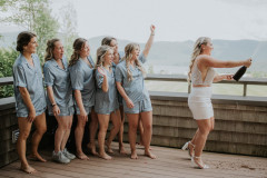 bride in white dress popping champagne while 6 bridesmaids in blue satin pajamas look on.