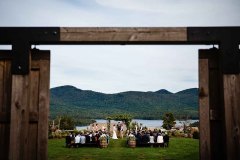 A knoll in the summer with a wedding ceremony seen through open barn doors.