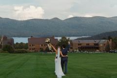 bride and groom walking towards the lodge with lake and mountains in the background with hands up.