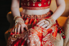 close-up of a woman's waist, arms and lap - dressed in red and gold Indian garb with a bare midrift.