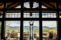 White wedding dress standing indoors in front of large windows overlooking patio with mountains and lake in background at Mountain Top Inn & Resort in Chittenden, VT