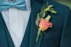 close-up of a man's blue suit with light blue bowtie and single peach colored rose boutonniere.