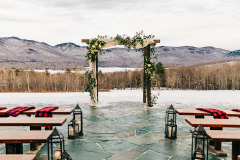 Wedding arch with flowers on it in front of empty seats with scarves and lanterns on seats with snowy mountain in background at Mountain Top Inn & Resort in Chittenden, VT