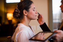photo of brunette woman in white shirt with hair in up-do,  having make-up done.
