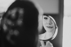 close up black and white photo of woman (from behind) looking into handeld mirror.