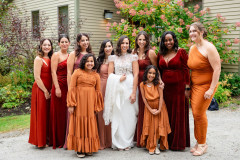 photo of bride and bridesmaids in orange dresses standing in front of house.