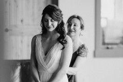 mother of bride zipping up dress while bride looks forward. photo is black and white.