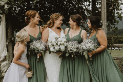 bride and bridesmaids in green dresses all looking at each other.