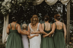 bride and bridesmaids in green dresses facing wedding knoll together.