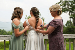 bride getting buttoned up by bridesmaid and mother of bride while facing away towards mountains