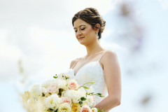 bride holding bouquet of white and pink florals in front of skylit background.