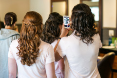 two women standing with their back to the camera , wearing pink shirts and holding a cellular phone taking a photo