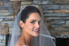 brunette bride with white veil standing in front of stone fireplace