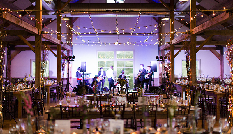 venue in barn with wooden beams with tables and chairs underneath, set with glassware with band playing on stage at Mountain Top Inn & Resort in Chittenden, VT