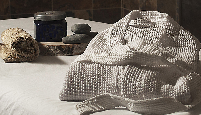 white robe on massage table beside warming pebbles and blue product jar