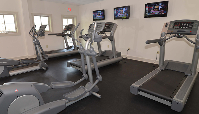 4 treadmills in a room with padded gym floors, windows facing flatscreen tvs on a white wall